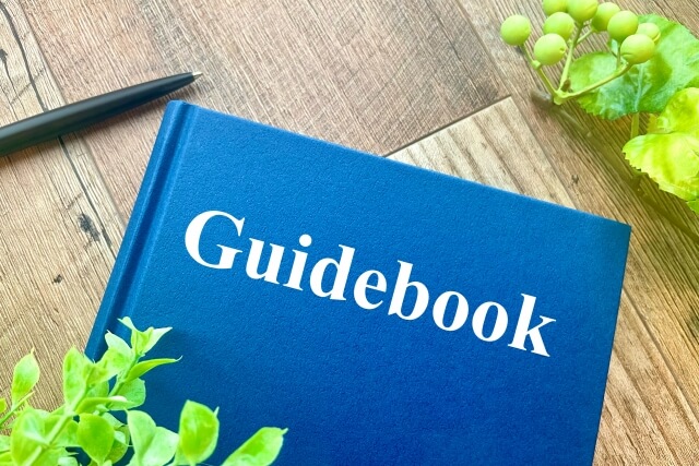 木の机に置かれた青い表紙の「Guidebook」と観葉植物